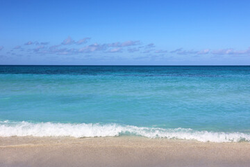 Tropical beach with white sand on a ocean, view to azure waves and sky with clouds. Caribbean coast, Background for holidays on a paradise nature