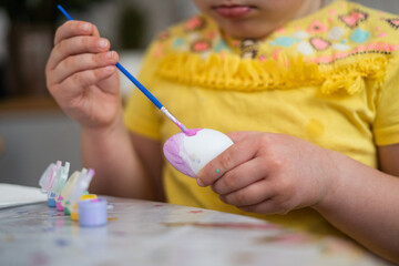 Child girl of preschool age painting Easter eggs at home kitchen. Easter spring traditions. Slow motion