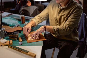 young talented craftsman marks holes in the leather, close up cropped side view shot