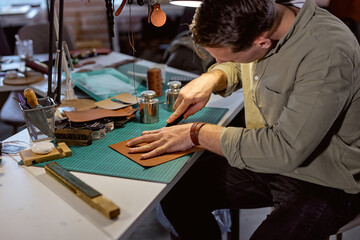 young active man sewing leather wallet, close up side view shot, guy prepare material for sewing, stitching