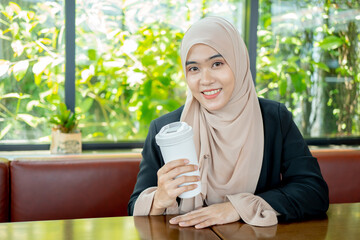 Asian Muslim woman cute Islam sitting and drinking coffee in a cafe with a happy face