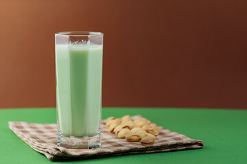 Healthy pistachio milk on a green-brown background. Vegan milk made from pistachios in a tall glass on a linen napkin. Copy space