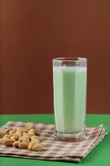Healthy pistachio milk on a green-brown background. Vegan milk made from pistachios in a tall glass on a linen napkin. Copy space