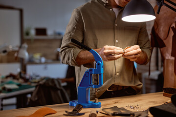 machine for doing embossed logo letters on leather product that heats the cliche and squeezes the desired image on the material , working artisan in the background of the photo. close up cropped shot