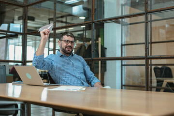 Happy male office worker enjoying break from work, throwing paper plane