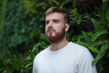 Portrait of happy young bearded man with beard breathing deep, inhale fresh air on natural background, green wall with leaves, flower in tropical country in garden. Eco, ecological concept. 