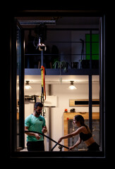 Fototapeta na wymiar Fit girl with exercising with ropes with a male fitness instructor in a fitness studio. View from outside the window.