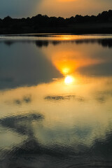 Beautiful sunset. The setting golden sun is reflected in the water surface on the lake. Vertical