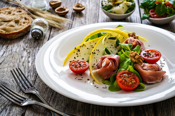 Tasty salad - prosciutto crudo, melon and fresh vegetables on wooden table

