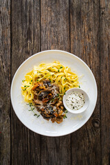 Tagliatelle with fried chicken breast nuggets, parmesan cheese and white mushrooms served on wooden table
