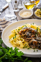 Tagliatelle with fried chicken breast nuggets, parmesan cheese and white mushrooms served on wooden table
