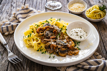Tagliatelle with fried chicken breast nuggets, parmesan cheese and white mushrooms served on wooden table
