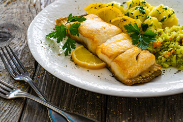 Fish dish - fried halibut with boiled potatoes and cabbage salad on wooden table