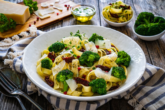 Pasta with broccoli, parmesan and sun dried tomatoes on wooden table
