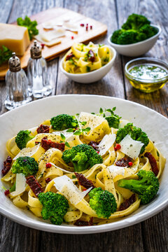 Pasta with broccoli, parmesan and sun dried tomatoes on wooden table

