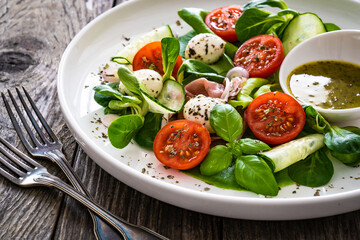 Fresh salad - prosciutto di Parma, mozzarella, cucumber, tomatoes and leafy vegetables on wooden table
