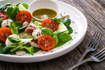 Fresh salad - prosciutto di Parma, mozzarella, cucumber, tomatoes and leafy vegetables on wooden table
