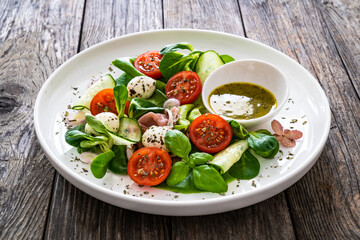 Fresh salad - prosciutto di Parma, mozzarella, cucumber, tomatoes and leafy vegetables on wooden...