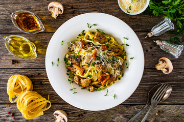 Tagliatelle with fried chicken breast nuggets, parmesan cheese and white mushrooms served on wooden table 