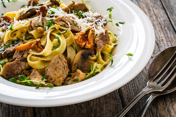 Tagliatelle with fried chicken breast nuggets, parmesan cheese and white mushrooms served on wooden table 