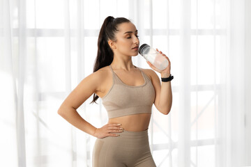 Fototapeta na wymiar Athletic lady drinking water while exercising at home