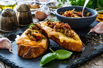 Tasty sandwiches - baked bread with cheese, olives, sun dried tomatoes and thyme on wooden table
