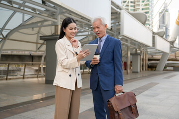Fototapeta premium Asian senior mature middle aged businessman and young businesswoman having a discussion and using tablet in modern city