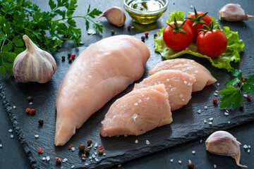 Fresh raw chicken fillet on cutting board with spices on black background
