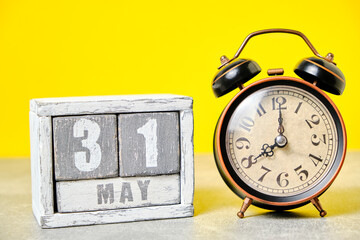 May 31 on a wooden calendar and an old retro alarm clock on a yellow background.