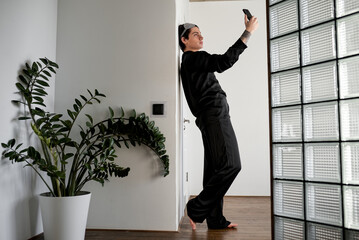 handsome egoist holding cell phone looking at the screen, taking photo, standing indoors, full...