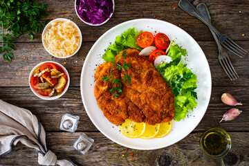 Breaded fried pork chop with cabbage salad and greens on wooden table
