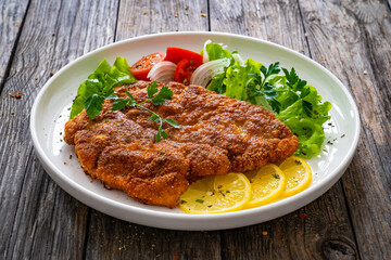 Breaded fried pork chop with cabbage salad and greens on wooden table
