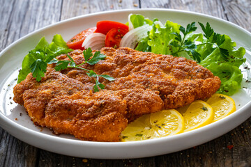 Breaded fried pork chop with cabbage salad and greens on wooden table
