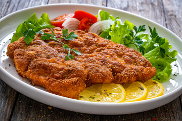 Breaded fried pork chop with cabbage salad and greens on wooden table
