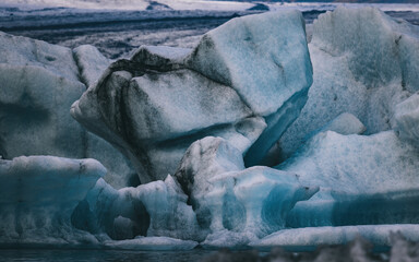 Fototapeta na wymiar Abstract shapes of blue icebergs in the Jokulsarlon glacial lagoon, Southern Iceland. Part of the Vatnajokull National Park. Black layers are volcanic ash. Muted tones.