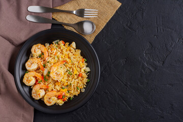 Fried rice with vegetables and prawns in a black plate. Laying on the table. Black background- top view.