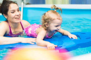 Obraz na płótnie Canvas Happy kid learning to swim with mom in the pool