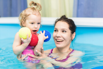 Happy baby girl swims in the pool with her mother