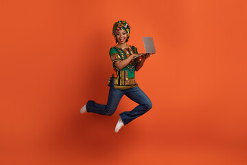 Happy traditional african woman jumping with open laptop