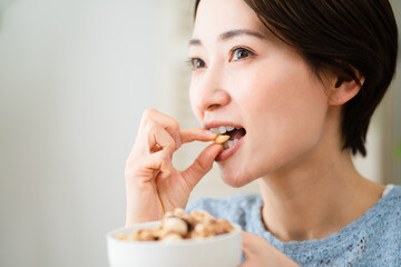 ミックスナッツを食べる若い女性　飲食イメージ - obrazy, fototapety, plakaty