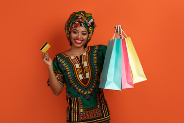 Cheerfy black lady showing colorful shopping bags and bank card
