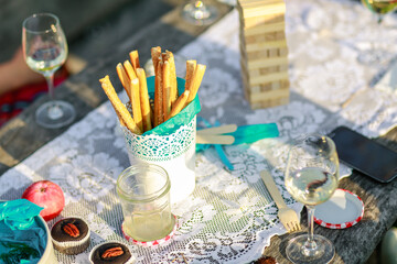 Salty chip stick snacks, board game and white wine glass on a picnic table in summer