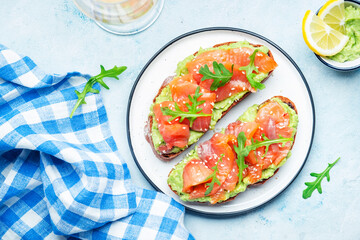 Avocado and salmon sandwich on rye bread with guacamole sauce, arugula and sesame seeds on plate,...