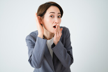 耳に手を当てて噂話を聞く若い女性　ビジネスイメージ