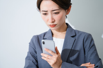 スマートフォンを持ちながら悩んでいる若い女性　ビジネスイメージ