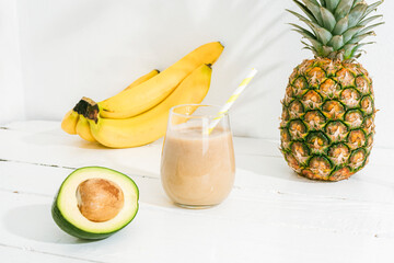 Banana, pineapple and avocado smoothie on white wooden table in sunlight. Minimal detox diet concept, summer vitamin drink