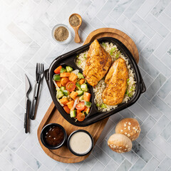 A meal consisting of chicken breasts with rice, salad, barbeque sauce, flour, and bread.Top View