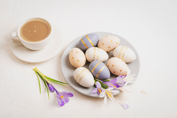 Gray plate with painted Easter eggs, coffee cup and crocus flowers on white background. Easter...