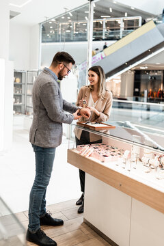 Elegant middle age businessman choosing and buying his new expensive watch. Beautiful young female seller helps him to make good decision. Fashion style and elegance concept.