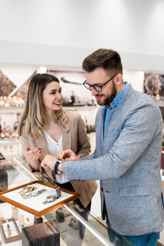 Elegant middle age businessman choosing and buying his new expensive watch. Beautiful young female seller helps him to make good decision. Fashion style and elegance concept.